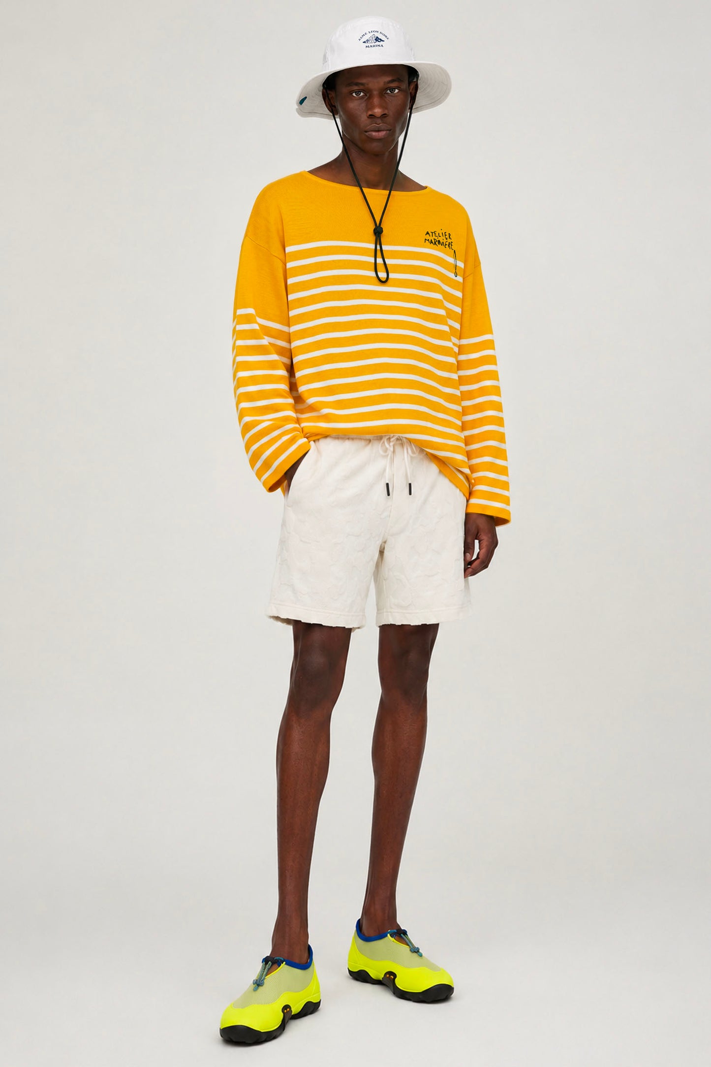 Model wearing Atelier Marinière's oversized yellow Breton shirt with white shorts, handcrafted in Italy from premium cotton