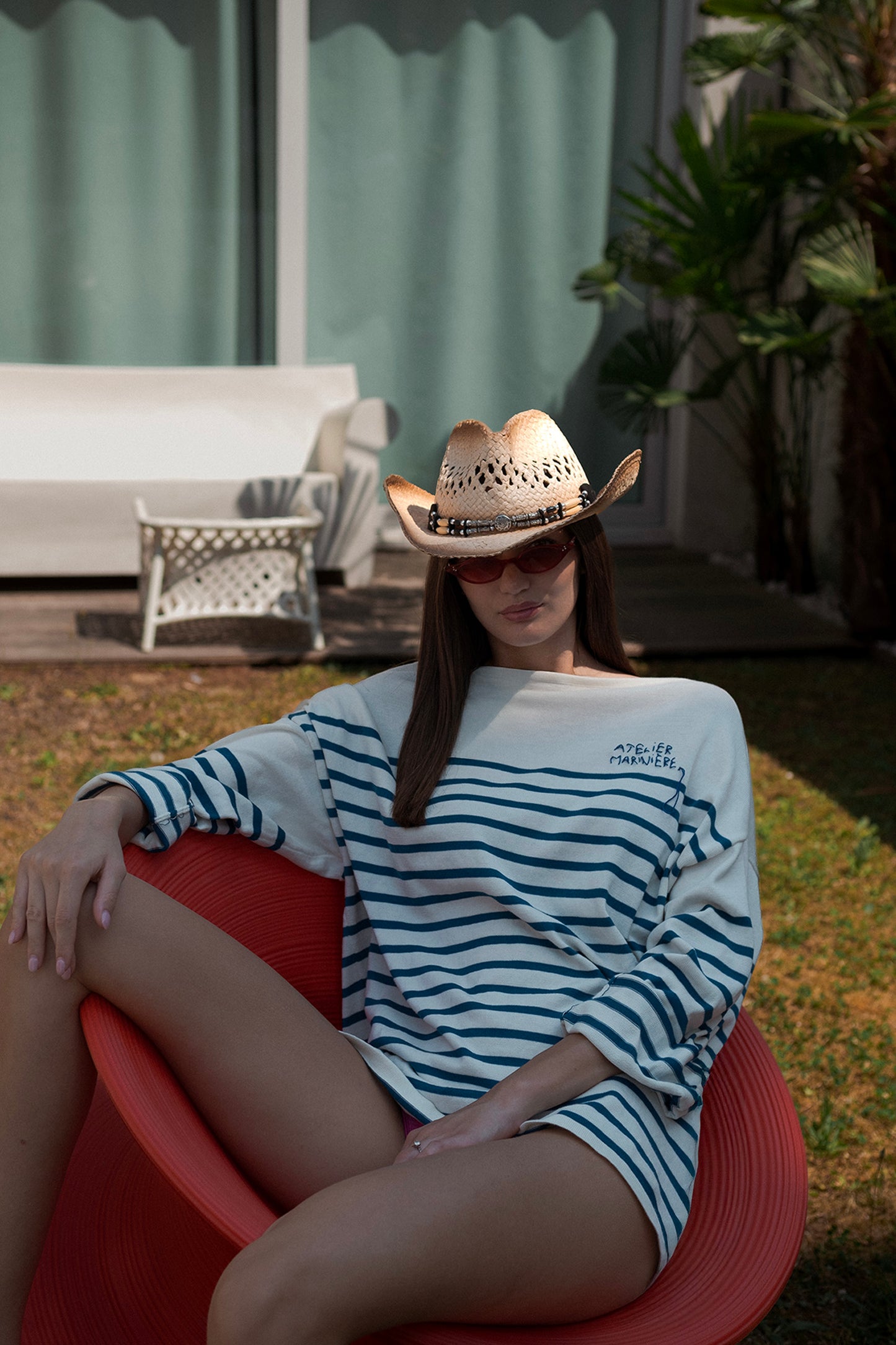 Woman wearing Atelier Marinière's oversized white and blue Breton shirt in a relaxed summer setting, handcrafted in Italy from premium cotton