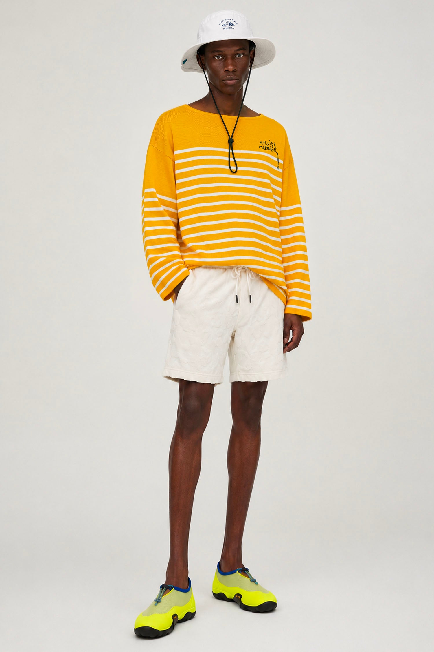 Model wearing Atelier Marinière's oversized yellow Breton shirt with white shorts, handcrafted in Italy from premium cotton