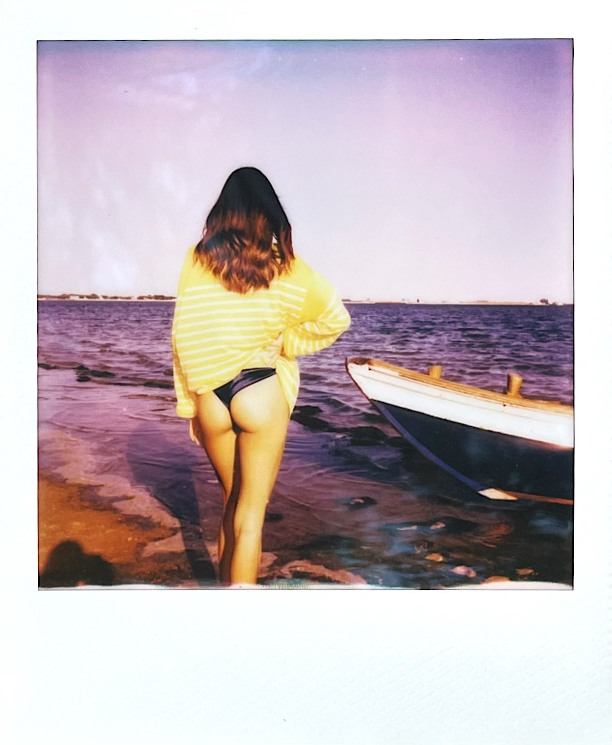Polaroid of a woman wearing a yellow Breton shirt by Atelier Marinière on the beach beside a boat in the Venetian lagoon.